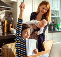 Woman holding baby watching son on laptop doing homework